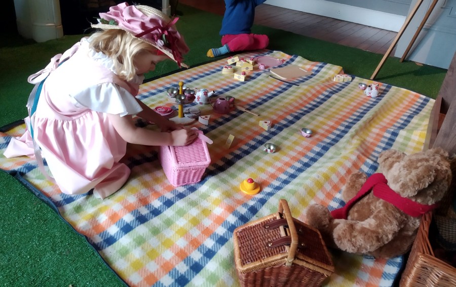 Child playing with toy cakes and a pink picnic hamper